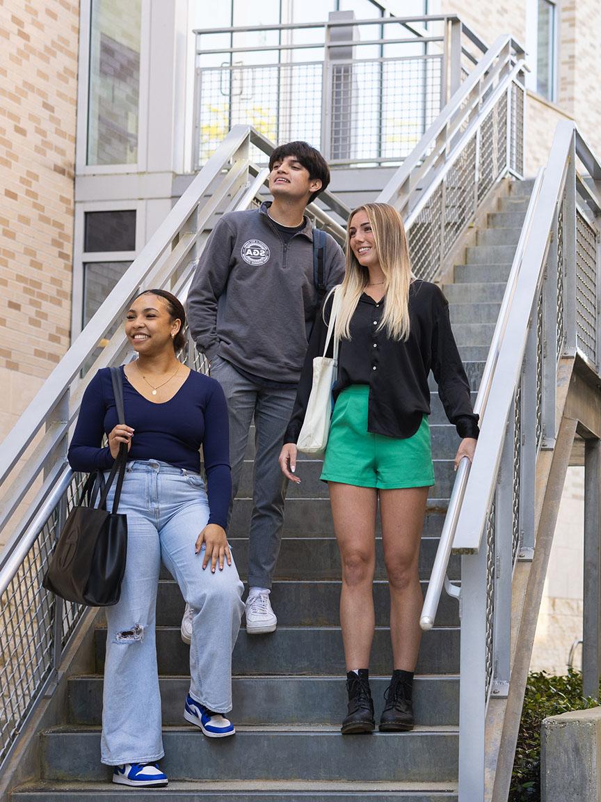 Three UWF students descend outdoor stairs on campus.