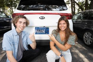 两个学生跪在一辆挂着Argos车牌的汽车后备箱前